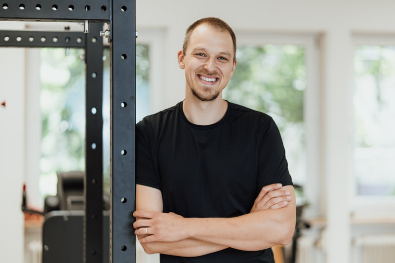 Portrait von Jan von corpus et animus lachend in schwarzem T-Shirt gegen ein Rack gelehnt